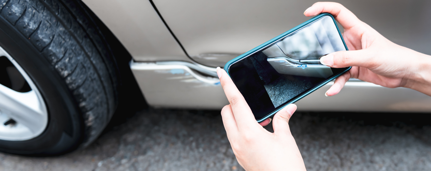 Person fotografiert einen Schaden am Auto mit dem Smartphone
