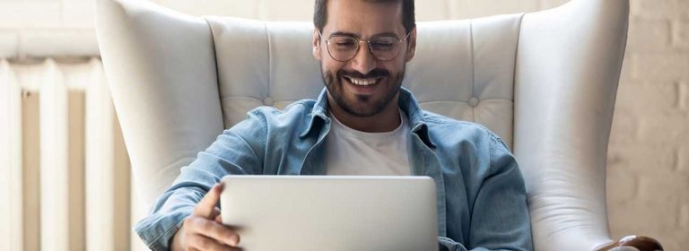 Mann sitzt mit Laptop in einem Couchsessel