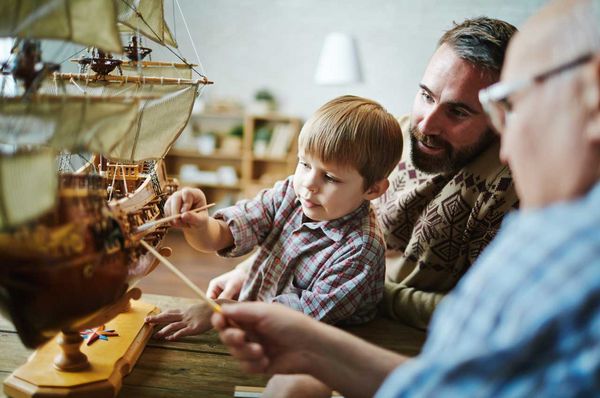 Großvater, Vater und Sohn spielen gemeinsam mit einem Modellschiff
