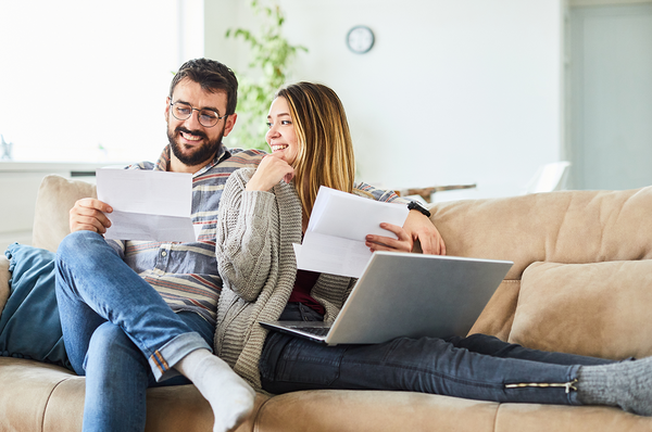 Pärchen sitzt auf der Couch und hält Dokumente in den Händen