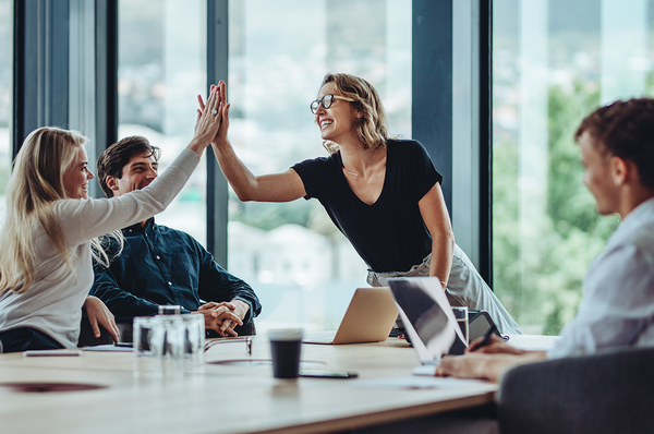 Team sitzt an Tisch und zwei Personen geben sich ein High-Five