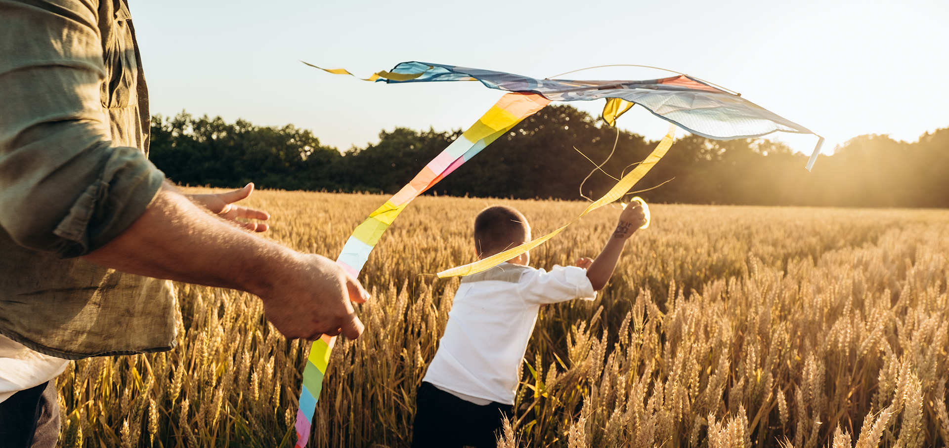 Kind läuft bei Sonnenuntergang mit einem Drachen durch ein Weizenfeld