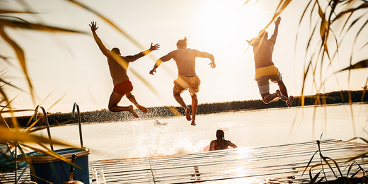 Drei Personen springen vom Steg ins Wasser.