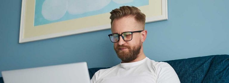 Mann sitzt auf einer Couch und arbeitet am Laptop