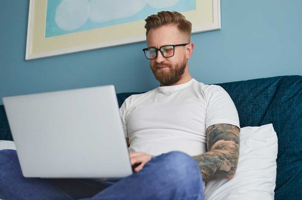 Mann sitzt auf einer Couch und arbeitet am Laptop