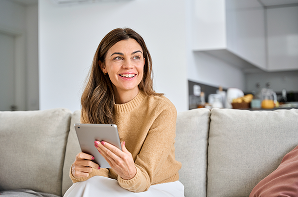 Junge Frau sitzt auf dem Sofa und informiert sich am Tablet über die Vorsorgemöglichkeiten für Frauen