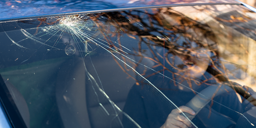 Frau am Steuer sieht erschrocken den Steinschlag in der Windschutzscheibe ihres Autos.