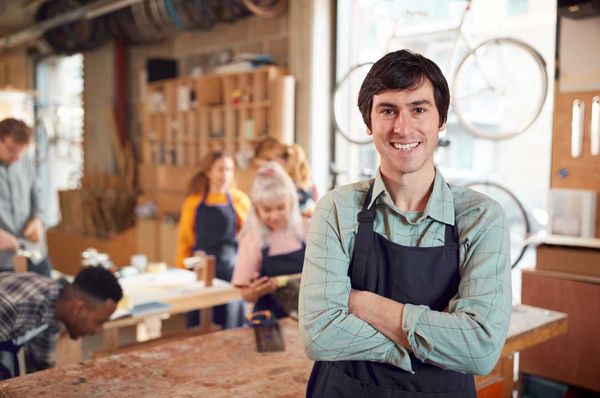 Mann in Latzhose steht mit verschränkten Armen in einer Werkstatt
