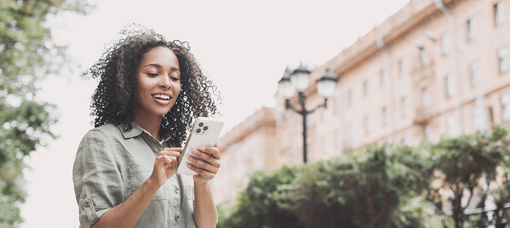 Junge Frau steht in der Stadt und hält Handy in den Händen