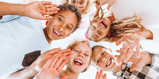 Eine Gruppe lachender Kindern steht im Kreis und winkt in die Kamera