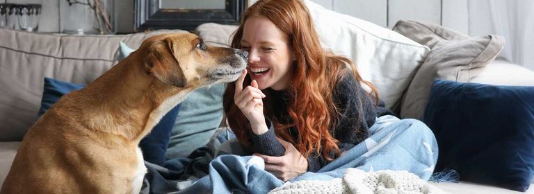 Frau sitzt gemeinsam mit ihrem Hund auf der Couch