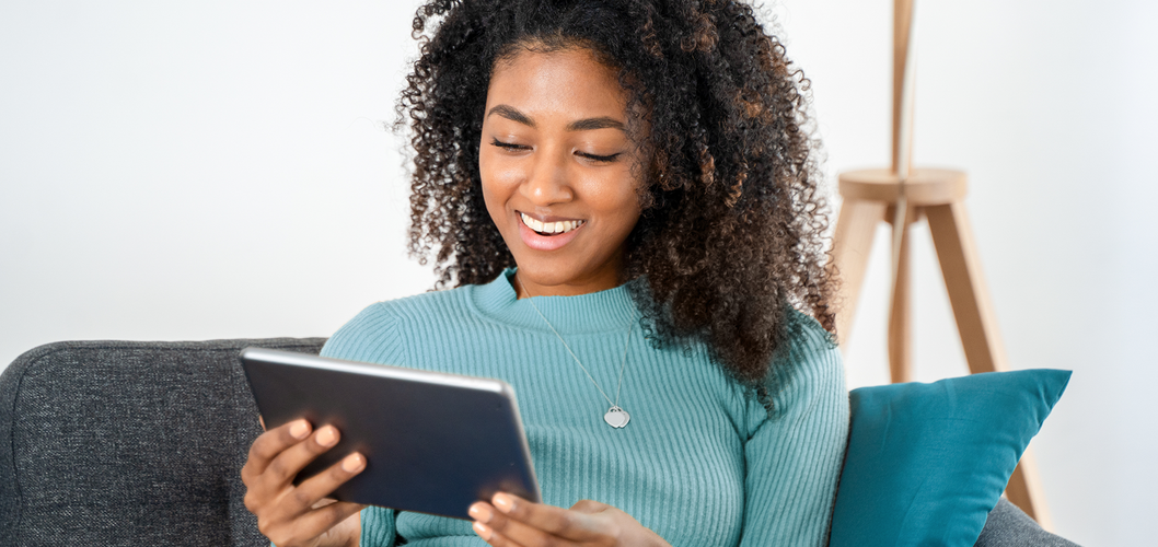 Junge Frau sitzt auf Couch und hält ihr Tablet in den Händen