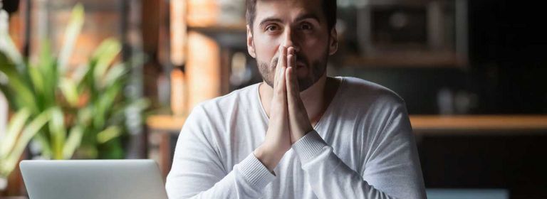 Mann sitzt mit gefalteten Händen vor dem Laptop