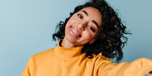 Selfie einer dunkelhaarigen jungen Frau mit gelben Pullover und weißen Zähnen