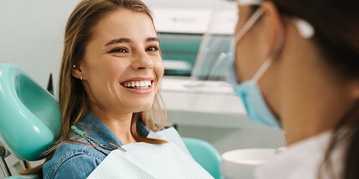 Junge Frau sitzt lächelnd im Zahnarztstuhl und bekommt eine professionelle Mundhygiene