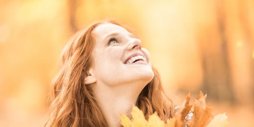Frau im Wald hält Laub in der Hand und lächelt
