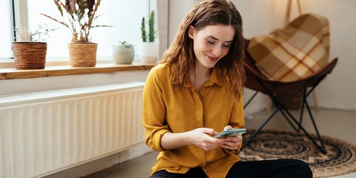 Junge Frau sitzt mit Handy am Boden vor einem Heizkörper