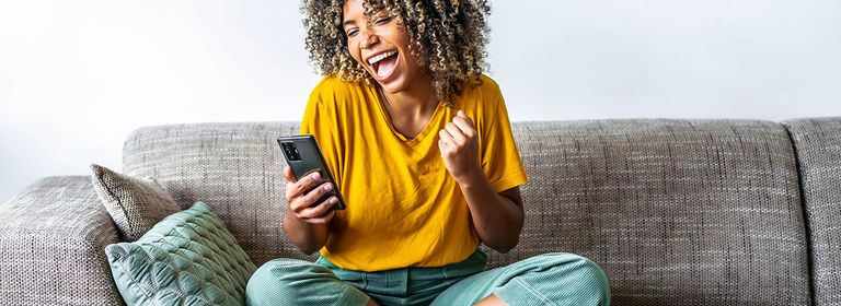 Junge Frau sitzt am Sofa mit Smartphone