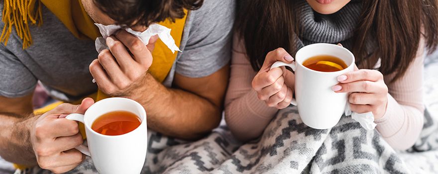 Erkältetes Pärchen sitzt mit Tee und Decke auf der Couch