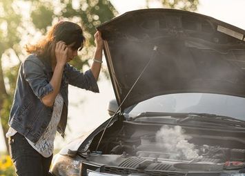 Frau steht bei defektem Auto am Straßenrand und telefoniert