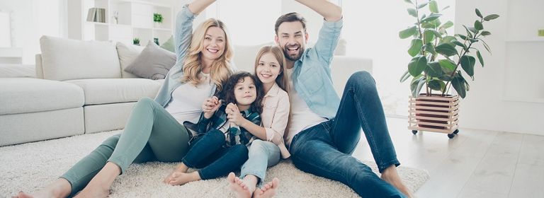 Familie mit zwei Kindern sitzen am Boden und die Eltern formen mit den Händen ein Dach über den Köpfen der Kinder, um Schutz des Privat-Rechtsschutzes zu symbolisieren