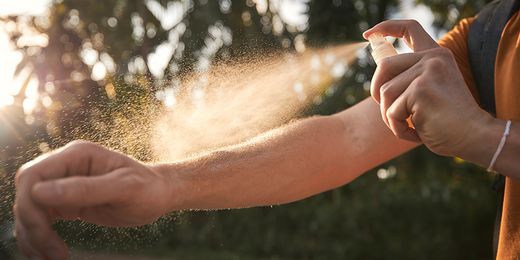 Person im Freien sprüht sich Mückenschutzspray auf die Arme