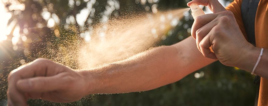 Person im Freien sprüht sich Mückenschutzspray auf die Arme